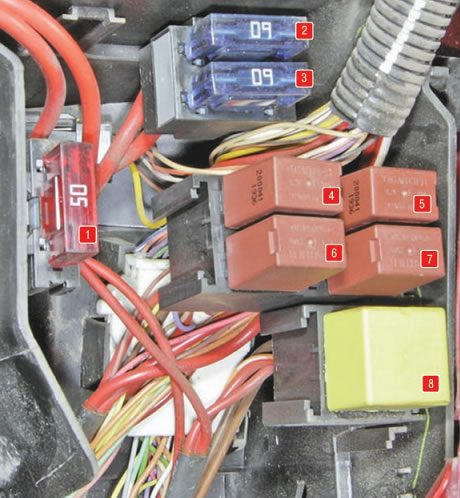 Pojistková skříňka v motorovém prostoru vedle baterie pod krytem.